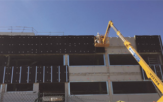 Operario de grúa instalando placas de lana mineral en una fachada ventilada